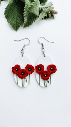 two red flowers are in the center of a pair of white dangle earrings with green leaves