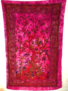 a pink and red tapestry hanging on a wall next to a white wall with a tree of life in the middle