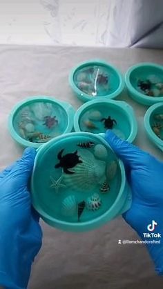 a person in blue gloves is holding a bowl with small fish inside it and several other bowls on the table