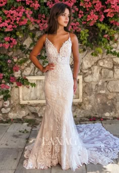 a woman in a wedding dress standing next to a stone wall with pink flowers on it