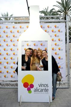 two women standing in front of a wine bottle with a photo frame on it's side