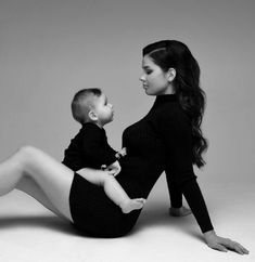 a woman is holding a baby while sitting on the floor