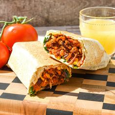 a burrito cut in half sitting on top of a cutting board next to tomatoes