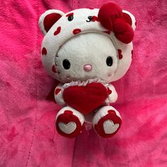 a hello kitty stuffed animal with a heart on it's chest sitting on a pink blanket