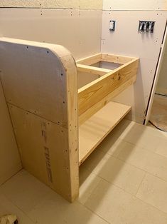 an unfinished wooden shelf in the corner of a room with tile flooring and white walls