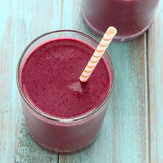 two glasses filled with red smoothie sitting on top of a blue wooden table next to each other