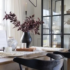 a dining room table with some vases and flowers on it, along with two chairs