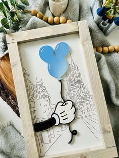 a wooden frame with a drawing of mickey mouse holding a blue balloon in front of a cityscape