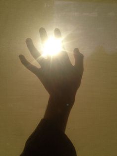 a person's hand reaching up towards the sun