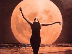 a woman standing on the beach with her arms outstretched in front of a full moon