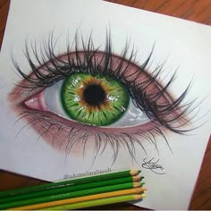 a drawing of an eye with green eyeshade and long eyelashes, surrounded by colored pencils