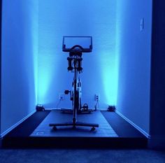 an exercise bike is illuminated by blue lights in a room with white walls and carpeted flooring