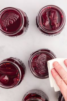 a hand wiping down the top of some jars filled with red liquid and another person holding a cloth over them