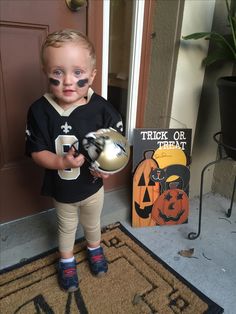 a little boy with his face painted like a jack - o'- lantern holding a football