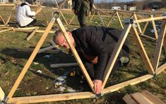 two men are working on wooden structures in the grass and one man is bending over