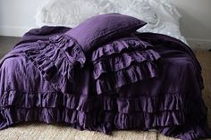 a bed with purple ruffled sheets and pillows