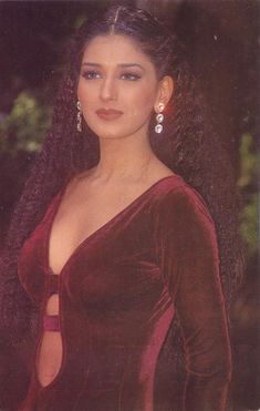 a woman with long hair wearing a red dress and dangling earrings, posing for the camera