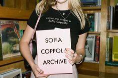 a woman holding up a sign that says sofia coppola archive in front of bookshelves