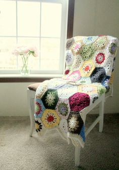 a white chair with a crocheted blanket on it in front of a window