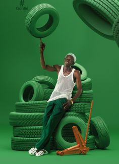 a man sitting on top of a pile of green tires holding up a large tire