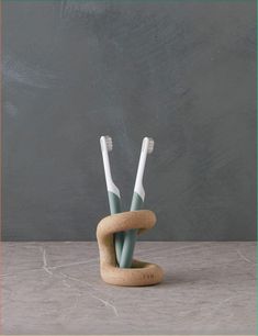 two toothbrushes are in a holder made out of cork and concrete, against a gray wall