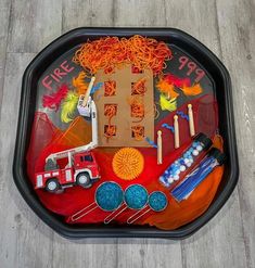 a tray that has various items in it on top of a wooden floor next to a fire truck