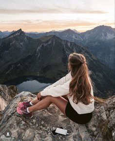 a woman sitting on top of a mountain next to a lake