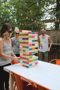 three people standing around a table with a giant block tower on it's side