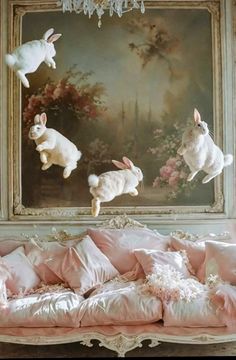 three white rabbits are jumping over a couch in front of a painting on the wall