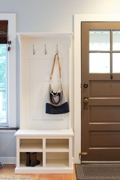 a white bench sitting in front of a door with a purse hanging on the wall