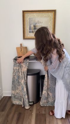 a woman is bending over to pick something out of the trash can in her house