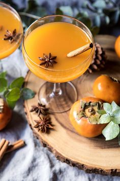 two glasses filled with orange juice sitting on top of a wooden tray next to cinnamon sticks