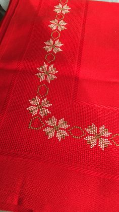 a red table cloth with white flowers and gold trimmings on the edge is sitting on a bed