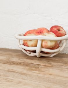 a white bowl filled with apples sitting on top of a wooden floor next to a wall