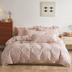 a bed with pink and white flowers on it in a room next to a dresser