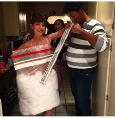 a woman in a white dress is wrapped in plastic and posing for the camera while another man looks on