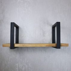 a wooden shelf with two black metal brackets on the top and bottom, against a gray wall