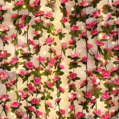 pink flowers with green leaves and lights on them are hanging from the ceiling in front of a white wall