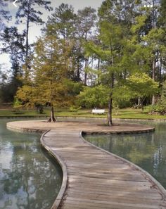 a wooden walkway that is next to a body of water with trees in the background