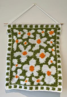 a crocheted wall hanging with an orange and white flowered design on it