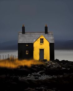 a yellow and black house sitting on top of a rocky beach