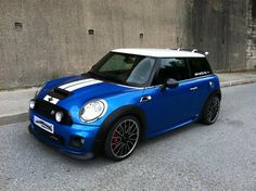 a blue mini with white stripes parked in front of a concrete wall on the street