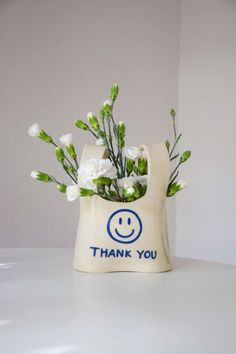 a white vase with flowers in it and the words thank you written on its side