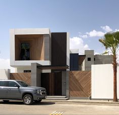 a car is parked in front of a modern house with wood and concrete sidings