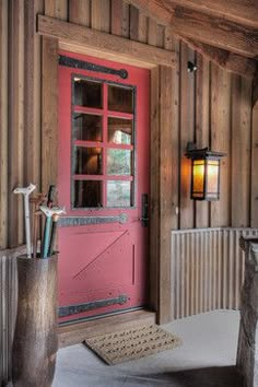 a red door in front of a wooden wall next to a lamp and some logs