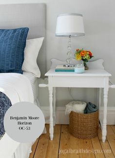 a small white table with flowers on it next to a bed and nightstand in a bedroom