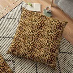 a leopard print floor pillow sitting on top of a rug next to a book and cup