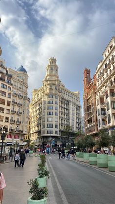 people are walking down the street in front of some very tall buildings with balconies