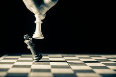 a person is playing chess on a checkerboard floor with their hand over the queen's pawn