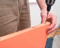 a man is using a drill to fix an orange piece of wood